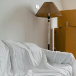 Covered with sheet sofa and floor lamp and packed cardboard boxes in light spacious room of new contemporary house