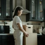 A woman standing in a kitchen unpacking cardboard boxes in a modern apartment.
