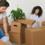 Serious young relocating man and woman in casual outfits packing fragile things into carton boxes while preparing for moving into new apartment in daylight