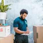 A mover with a clipboard checking packages and boxes for relocation indoors.